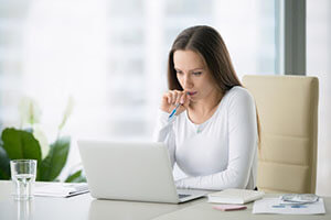 pensive woman sitting at the table in front of the computer